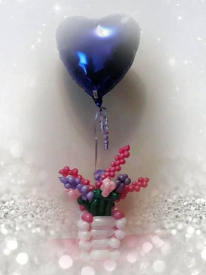 A small basked made of light pink balloons is filled with balloons contorted to resemble wild flowers. Floating in the middle of the flowers is a foil purple heart balloon.